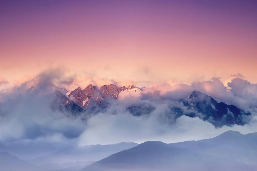 Berggipfel im Nebel bei Sonnenuntergang mit rosa und violettem Himmel