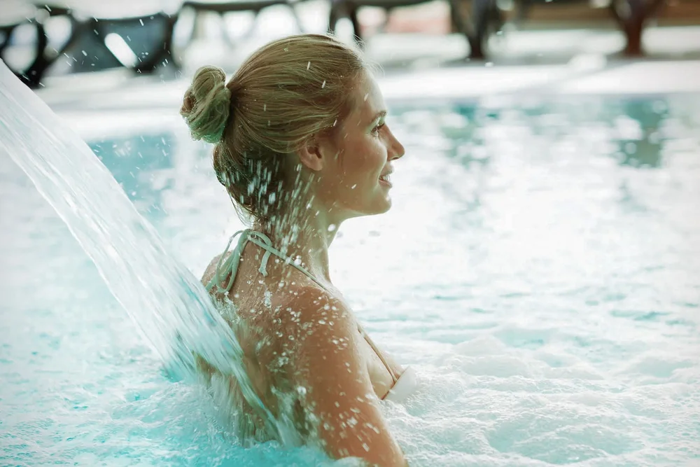 Frau entspannt im Pool unter Wasserstrahl