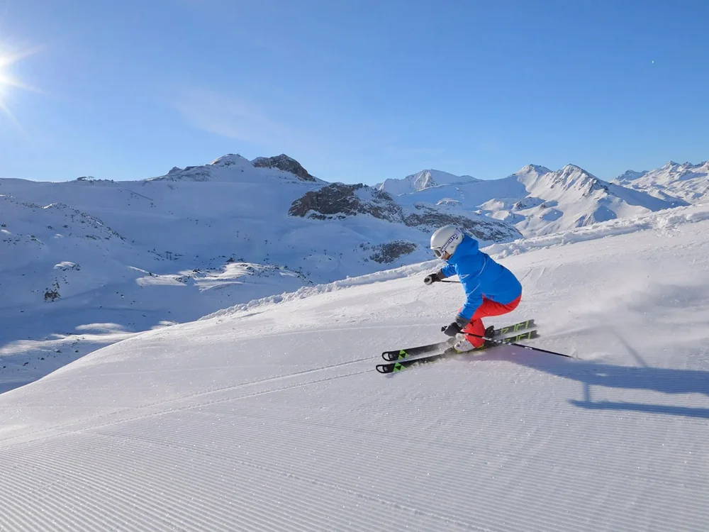 Hotel Salnerhof | 4 Sterne Superior in Ischgl Skifahrer in blauer Jacke fährt bei Sonnenschein auf frisch präparierter Piste