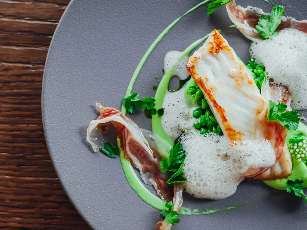 Hotel Salnerhof | 4 Sterne Superior in Ischgl Gourmetgericht mit Fischfilet, grünen Erbsen, Schaum und Kräutern auf grauem Teller