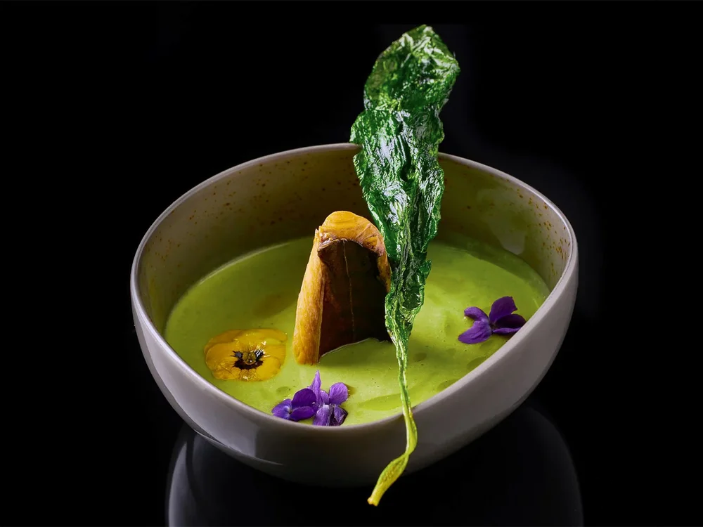Hotel Salnerhof | 4 Sterne Superior in Ischgl Grüne Suppe mit essbaren Blüten und knusprigem Blatt in weißer Schale