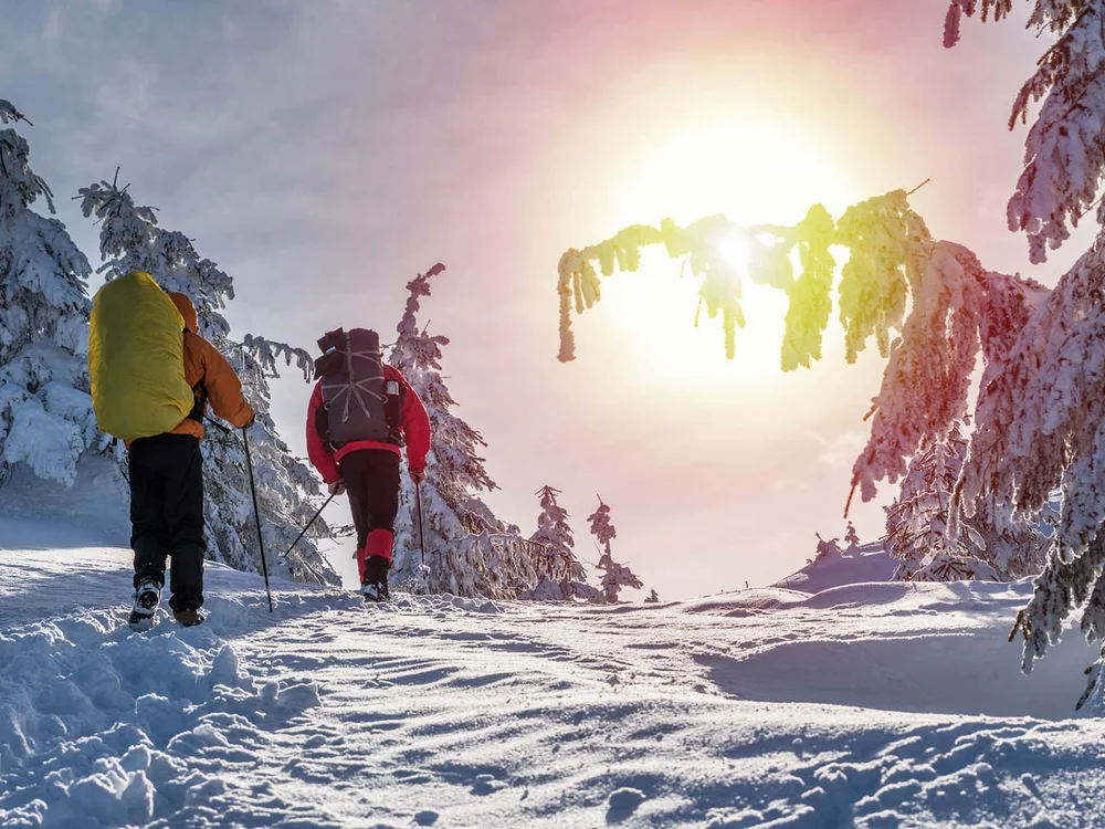 Hotel Salnerhof | 4 Sterne Superior in Ischgl Zwei Wanderer mit Rucksäcken wandern durch verschneite Winterlandschaft bei Sonnenschein