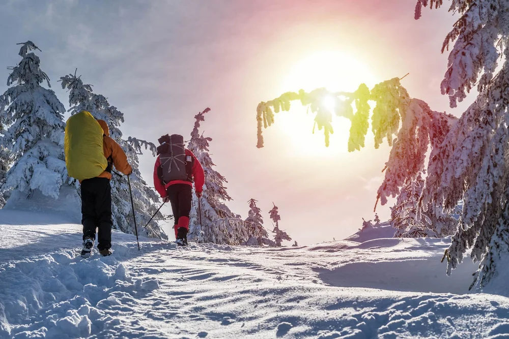 Zwei Wanderer mit Rucksäcken wandern durch verschneite Winterlandschaft bei Sonnenschein