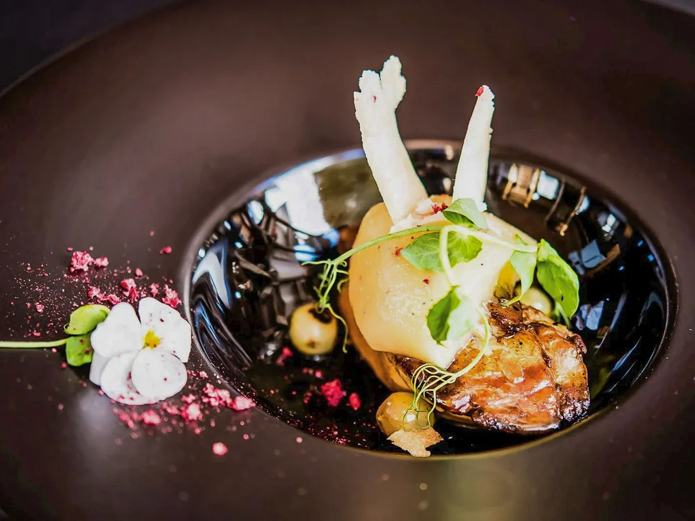 Hotel Salnerhof | 4 Sterne Superior in Ischgl Kunstvoll angerichtetes Gourmetgericht mit essbaren Blüten und Kräutern auf schwarzem Teller