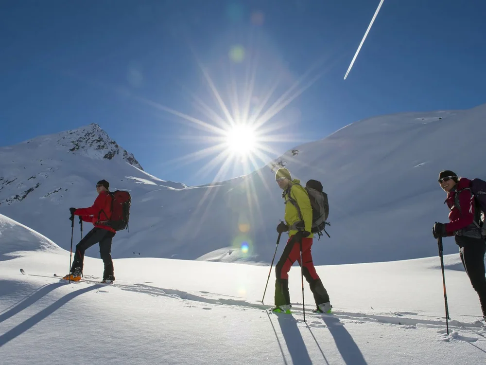 Hotel Salnerhof | 4 Sterne Superior in Ischgl Drei Skitourengeher wandern bei Sonnenschein durch verschneite Berge