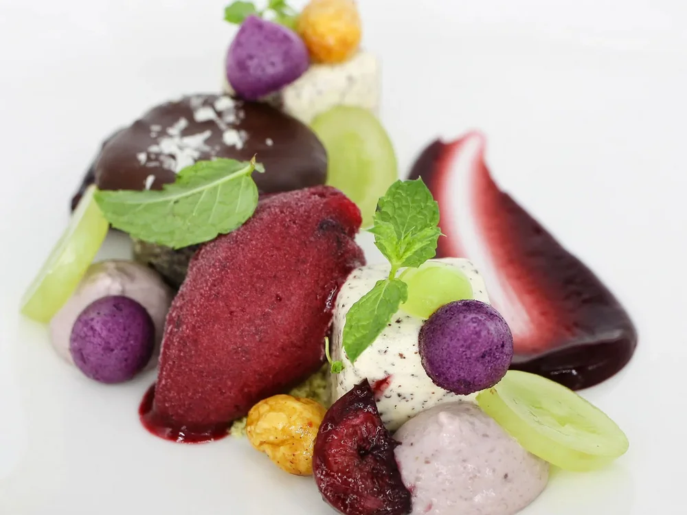 Hotel Salnerhof | 4 Sterne Superior in Ischgl Fein angerichtetes Dessert mit Beeren, Minzblättern und Fruchtsoße auf weißem Teller