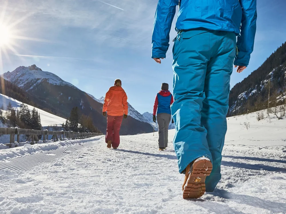 Hotel Salnerhof | 4 Sterne Superior in Ischgl Drei Personen wandern bei Sonnenschein auf verschneitem Bergweg
