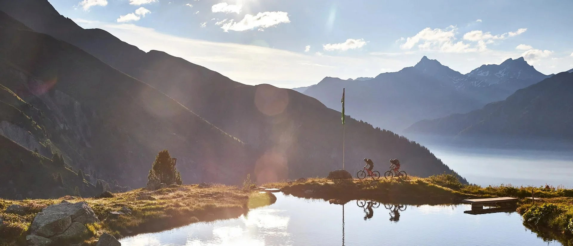 Hotel Salnerhof | 4 Sterne Superior in Ischgl Zwei Radfahrer fahren an einem Bergsee mit Bergpanorama bei Sonnenlicht