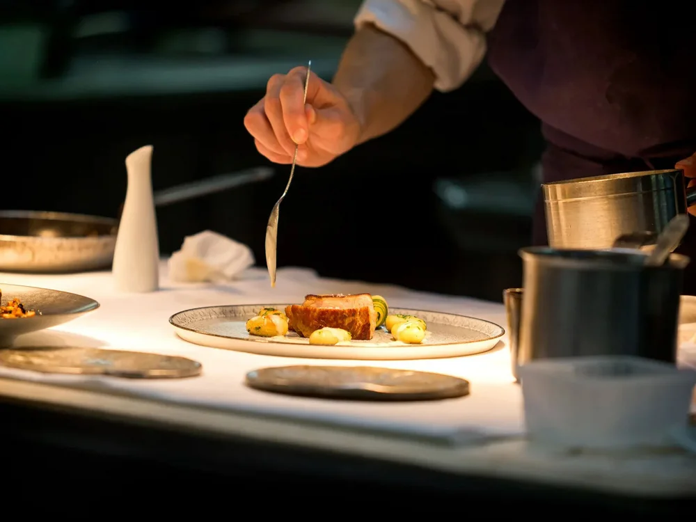 Hotel Salnerhof | 4 Sterne Superior in Ischgl Koch richtet ein Gourmetgericht auf einem Teller in einer Restaurantküche an